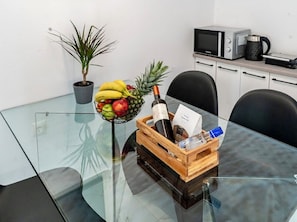 Uma mesa de vidro com uma fruteira, uma garrafa e um cesto de madeira com uma garrafa e um cartão.