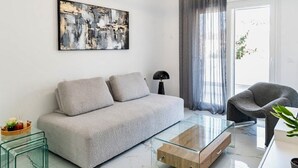 A modern living room with a grey sofa, a glass coffee table, a black floor lamp, and a grey armchair. - Sunny Nest Apartment 2 in Ixia (Ialisos)