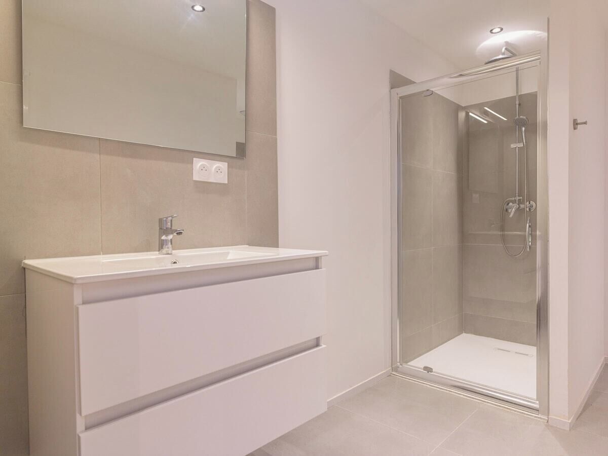 A modern bathroom with a glass-enclosed shower, a white vanity with a sink, and a mirror above the vanity.