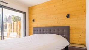 A bedroom with a large bed, a wooden headboard, and a sliding glass door leading to an outdoor area. - Apartment Le Cozy, high-end newly constructed! (Montgenèvre)