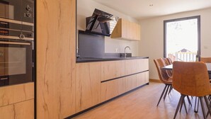 A modern kitchen with wooden cabinets, a built-in oven, and a dining area with a table and chairs. - Apartment Le Cozy, high-end newly constructed! (Montgenèvre)