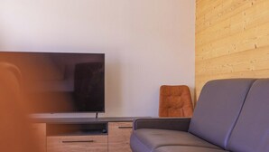 A modern living room with a flat-screen TV, a sofa, and a wooden accent wall. - Apartment Le Cozy, high-end newly constructed! (Montgen èvre)