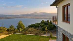 A modern building with a balcony overlooking a lake and distant mountains.