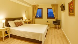 A hotel room with a bed, bedside tables, a chair, a small table, and a TV mounted on the wall.