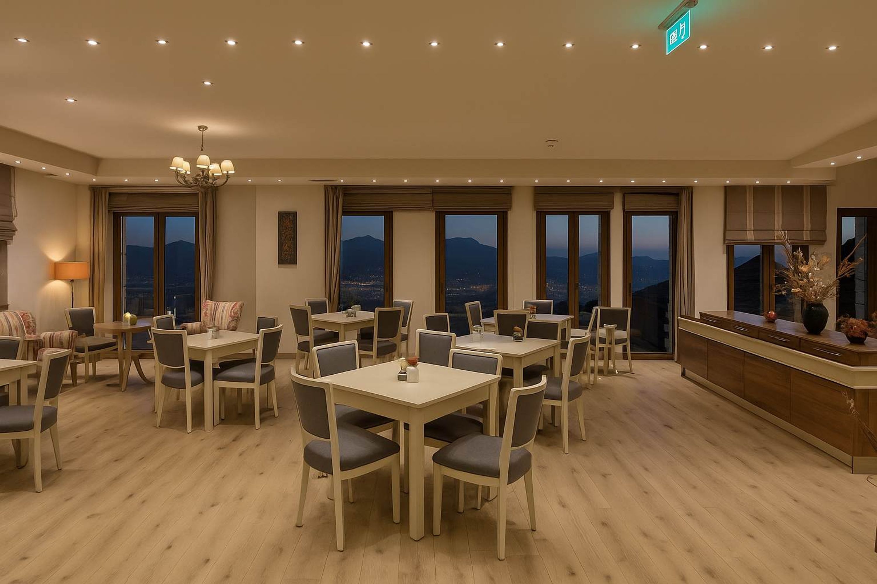 Un vaste espace dédié à la salle à manger, avec de nombreuses tables et chaises, de grandes fenêtres offrant une vue sur les montagnes et un lustre moderne.