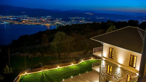Ein Haus mit einem Balkon mit Blick auf einen See und eine nächtliche Stadtansicht.