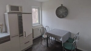 A compact kitchen with a white refrigerator, a microwave, and a dining table with chairs.