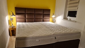 A bed with a padded headboard, two bedside lamps, and a window with blinds.