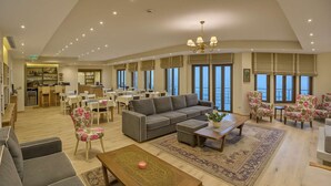 A spacious living area with a grey sofa, floral armchairs, a wooden coffee table, and a view of the sea through large windows. - Arktos Hotel Superior Room w/ Stunning Lake View (Ioannina)