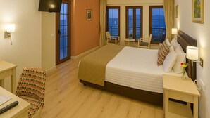 Habitación de hotel con una cama grande, un escritorio con una silla, un televisor montado en la pared y un balcón con vistas al mar.