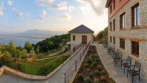 Un hotel con fachada de piedra, zona de estar al aire libre y vistas a un lago y montañas.