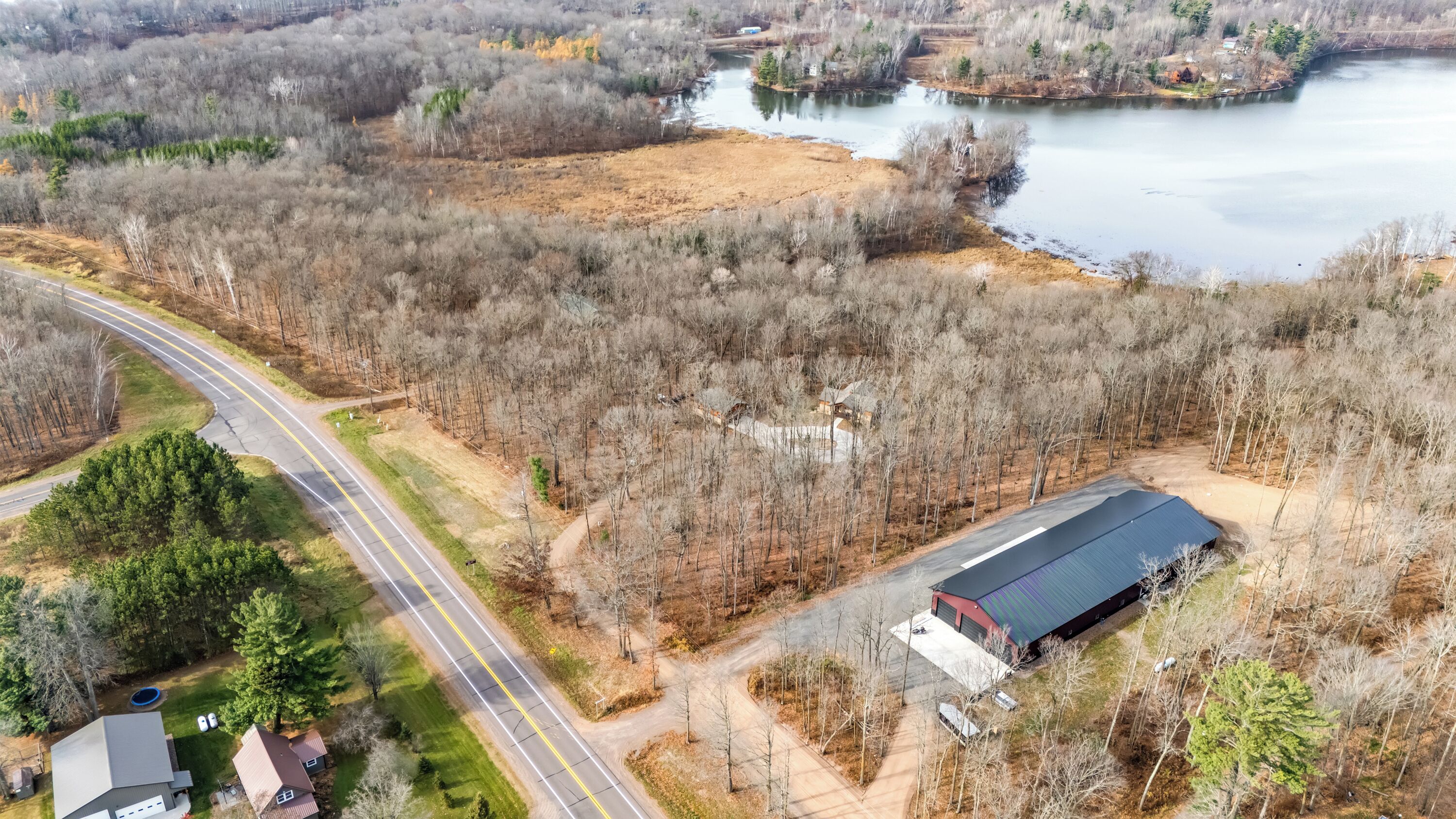An aerial view of a property with a large building, a road, and a lake.