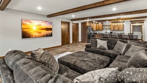 Ein modernes Wohnzimmer mit einer großen Eckcouch, einem Essbereich mit einem langen Tisch und einer Küche mit Holzschränken und einem Kühlschrank.