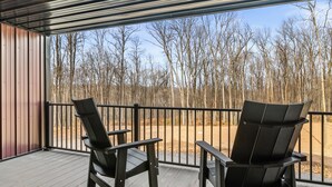 Eine überdachte Terrasse mit zwei schwarzen Stühlen und einem Metallgeländer.