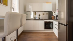 Une cuisine compacte avec des meubles blancs, un réfrigérateur en acier inoxydable et un four encastré.