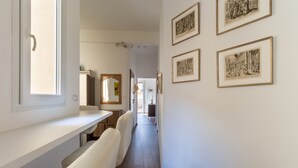 Un couloir avec un banc blanc, une fenêtre et des œuvres d’art encadrées accrochées au mur.