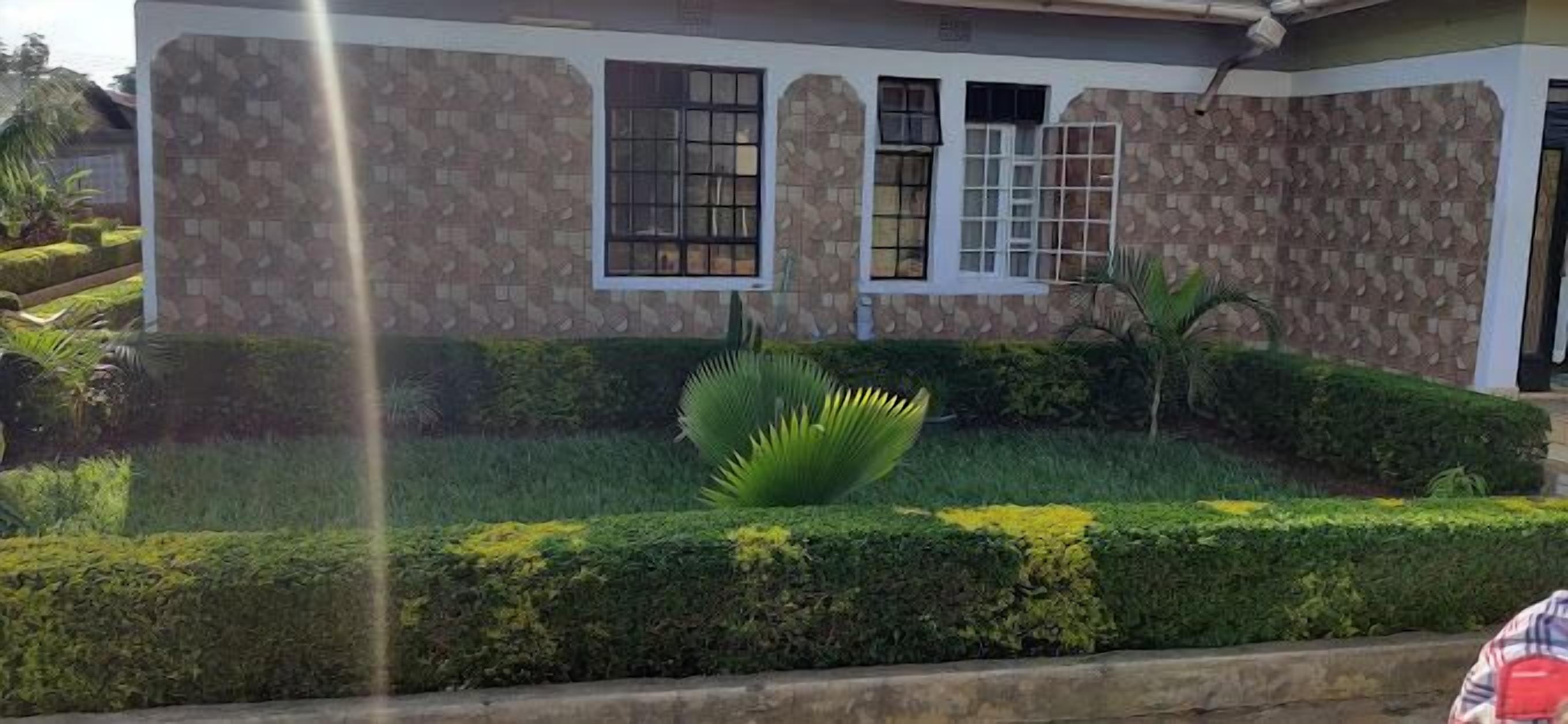 Un edificio de fachada de piedra, con múltiples ventanas y un jardín bien cuidado con setos y una palmera.