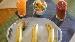 Ein Teller mit Bananen, eine Obstschale und zwei Getränke auf einem Tisch.