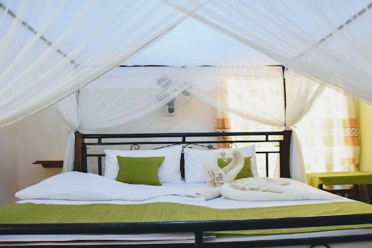 Ein Bett mit Moskitonetz, weißer Bettwäsche und einem grünen Kopfkissen.
