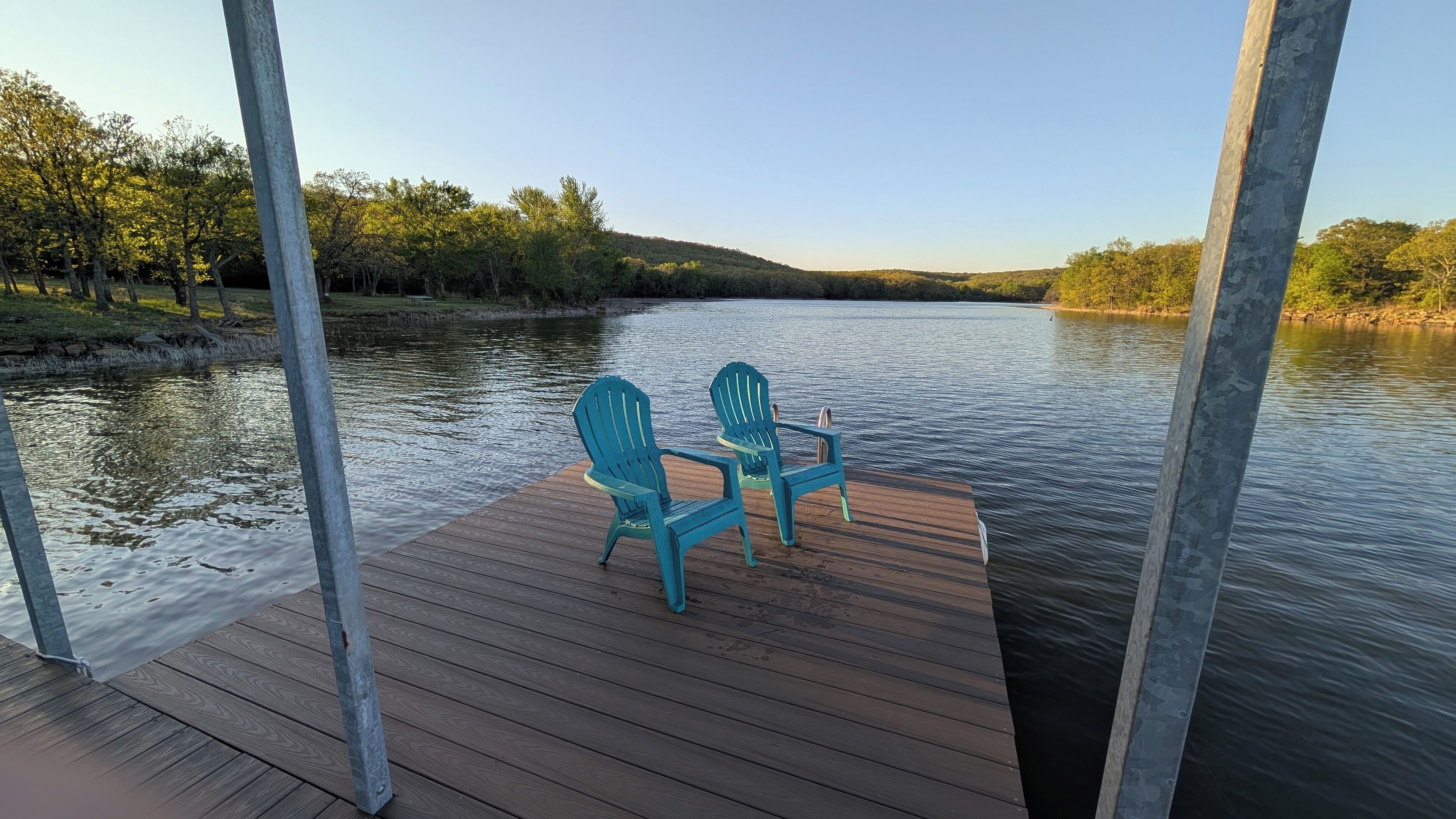 A wooden deck with two chairs and a table overlooking a calm river.