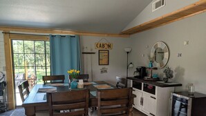 A dining area with a wooden table and chairs, a vase with flowers, and a kitchen area with cabinets and appliances.