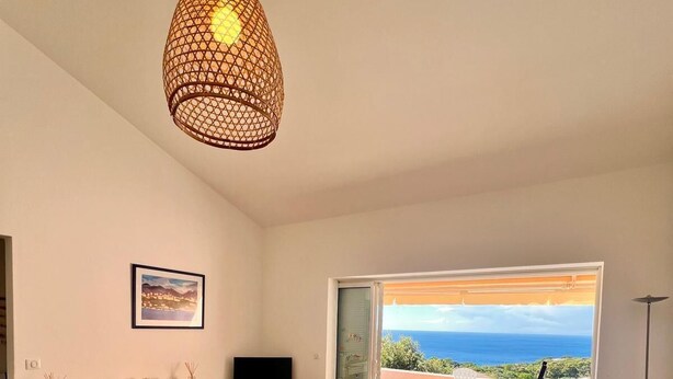Ett vardagsrum med en soffa, ett soffbord, en tv och utsikt över havet genom en skjutdörr.