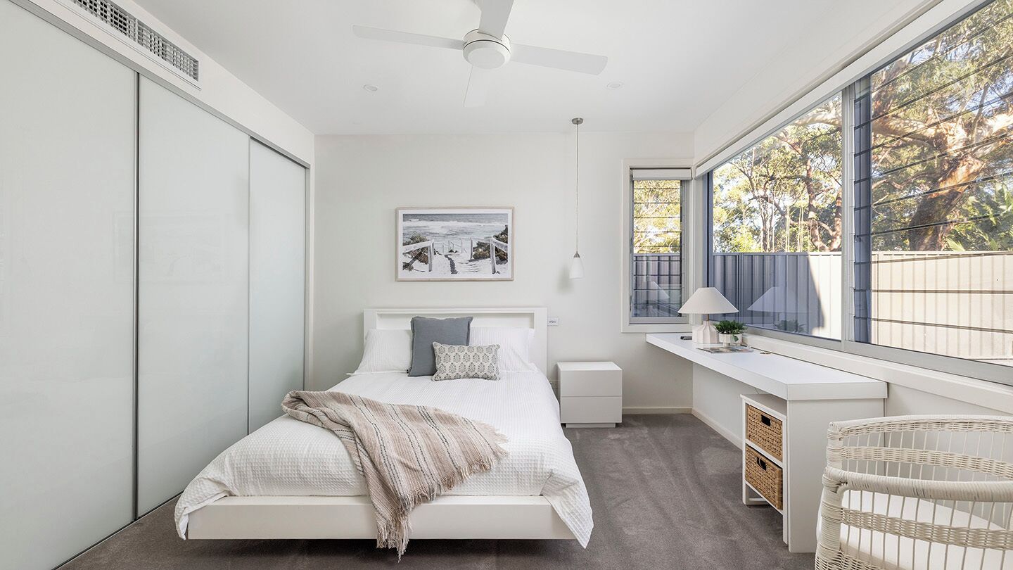A modern bedroom with a bed, bedside table, desk, and chair.