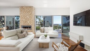 Una sala de estar moderna con chimenea de piedra, sofás blancos y un televisor grande.