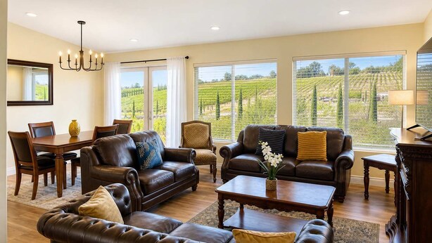 A spacious living room with leather sofas, a dining table, and large windows offering a vineyard view. - Private Temecula Getaway | Walk to Wineries (Temecula)