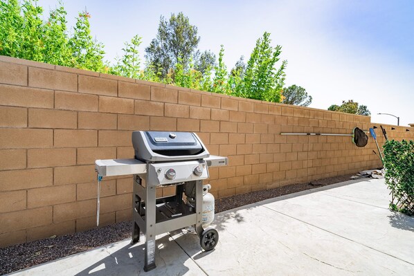 A portable barbecue grill with wheels, positioned against a brick wall on a concrete patio.