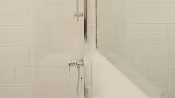 Een badkamer met een betegelde muur, een spiegel en een douche met een handdouche.