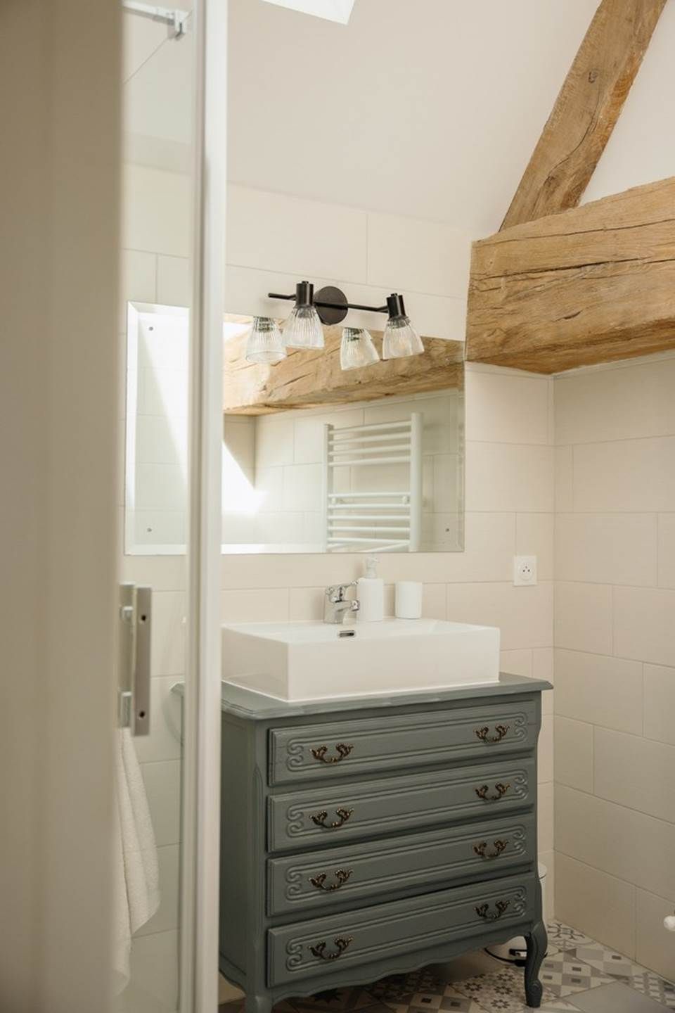 A bathroom with a white sink, a mirror, and a wooden ceiling beam.