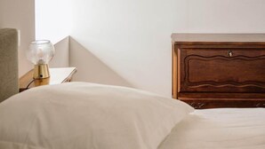 Un dormitorio con techo de madera, una mesita de noche con lámpara, cama con ropa de cama blanca y un espejo colgado en la pared.