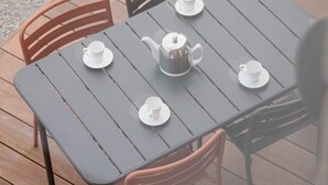 Una mesa cuadrada con cuatro sillas, una tetera y cuatro tazas sobre una terraza de madera.