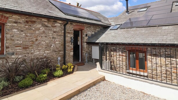 A stone building with a brick entrance, solar panels on the roof, and a gravel driveway. - Woodland Roost (Bideford)