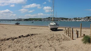 A sandy beach with a sailboat anchored near the shore, a clear blue sky, and a distant town with houses. - Woodland Roost (Bideford)