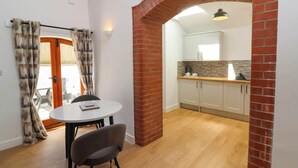 A dining area with a round table and chairs, a brick archway leading to a kitchen, and a view of the outside. - Woodland Roost (Bideford)