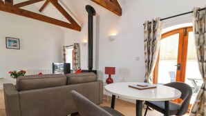 A modern living room with a sofa, chairs, a round table, a fireplace, and a window with curtains. - Woodland Roost (Bideford)