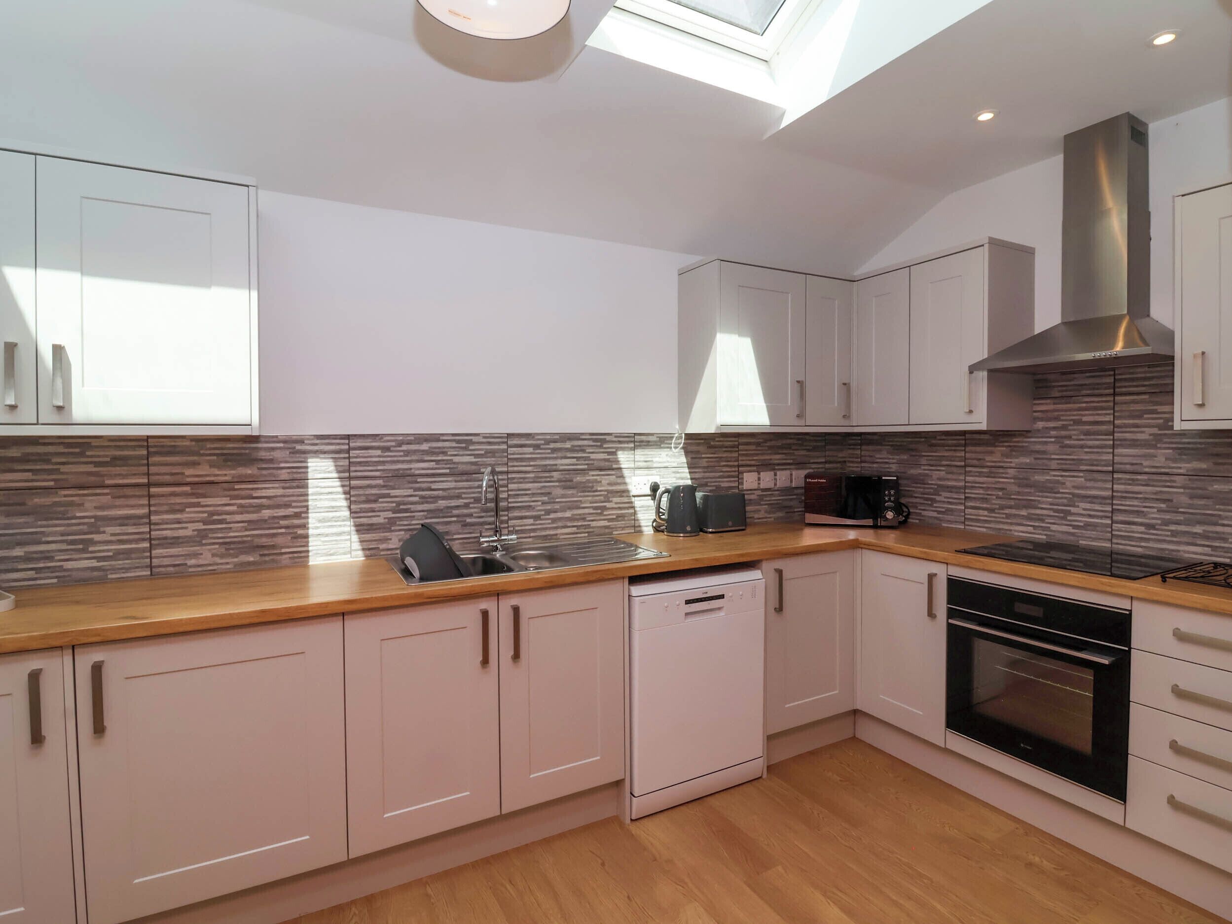 A modern kitchen with white cabinets, a wooden countertop, a built-in dishwasher, a microwave, a toaster, and an oven.