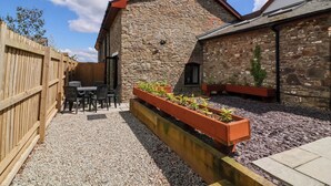 Un bâtiment en pierre doté d’une terrasse en bois et d’une cour en gravier.
