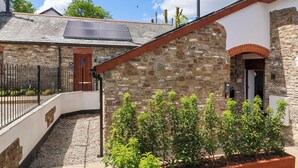 Un bâtiment en pierre avec un toit en pente, un petit jardin agrémenté de plantes en pot et une clôture en métal.