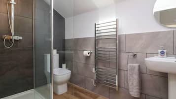 A modern bathroom with a glass shower enclosure, a toilet, a towel rack, and a sink with a mirror.