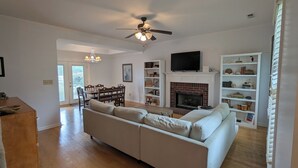 A spacious living room with a white sofa, a fireplace, a TV mounted above it, and a ceiling fan. - Moontown Magic (Huntsville)