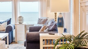 Un salon de style côtier, avec un ensemble de canapés, une lampe et une vue sur la mer.
