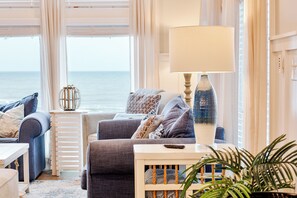 A coastal living room with a sofa set, a lamp, and a view of the sea. - Ocean Breeze: Oceanfront Pool & Hot Tub (Murrells Inlet)