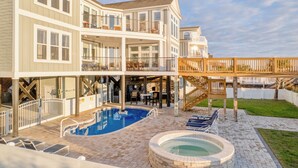 Une maison à deux étages dotée d’une piscine, d’un jacuzzi et d’une terrasse offrant une vue sur un plan d’eau.