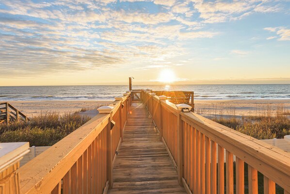 A wooden boardwalk leading to a beach with a sunset in the background. - Ocean Breeze: Oceanfront Pool & Hot Tub (Murrells Inlet)