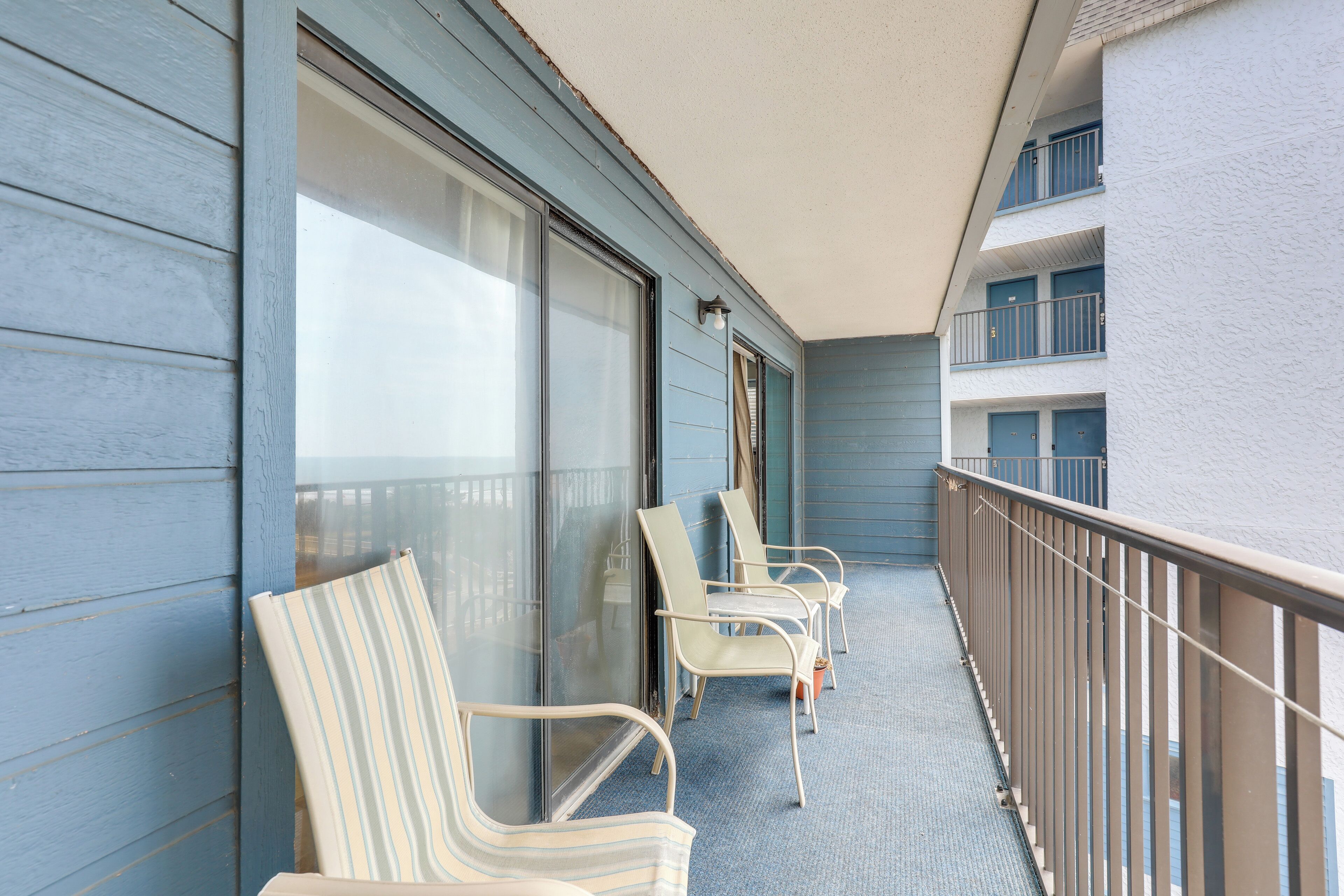 Un balcon avec quatre chaises à rayures et une table, une porte vitrée, et une vue sur la façade de l’immeuble.