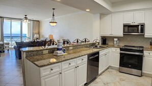 Una cocina moderna con gabinetes blancos, encimeras de granito, lavavajillas de acero inoxidable, microondas integrado y horno negro.