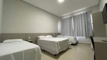 A hotel room with two single beds, a small bedside table, a flat-screen TV, and a window with curtains.